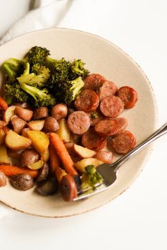 a plate with sausage, broccoli and carrots on it next to a fork