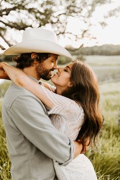 a man in a cowboy hat kissing a woman's forehead while standing in tall grass