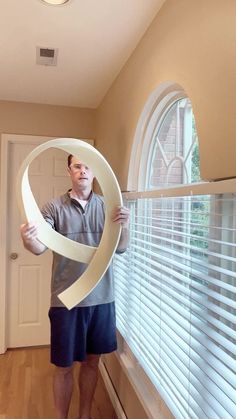 a man holding up a large white ribbon in front of a window with the letter o on it