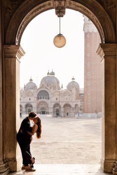 a man and woman kissing in front of a building with an arched doorway that leads into the courtyard