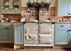 an old fashioned stove in the middle of a kitchen with blue cabinets and tile flooring