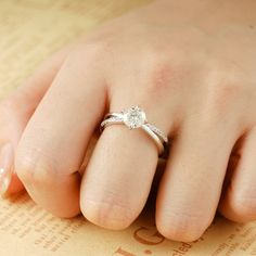 a woman's hand with a diamond ring on top of her finger and an old book in the background