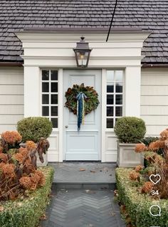 a white door with a wreath on it and some plants in the front yard next to it