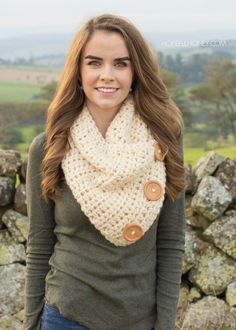 a woman standing in front of a stone wall wearing a white cowl with buttons on it