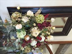 a vase filled with lots of flowers sitting on top of a wooden table next to a mirror