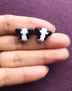 two small black and white cow earrings on someone's finger in a purple shirt