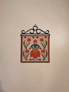 an embroidered wall hanging on the side of a white wall with a black metal frame