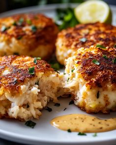 some crab cakes on a white plate with sauce and lemon wedges next to it