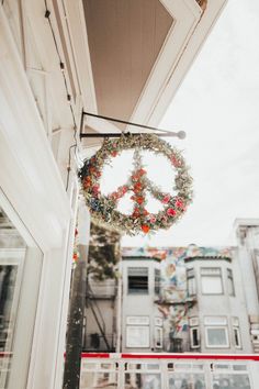 a peace sign hanging from the side of a building with flowers on it's front