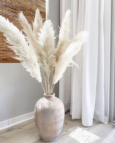 a vase filled with white flowers on top of a wooden floor next to a window