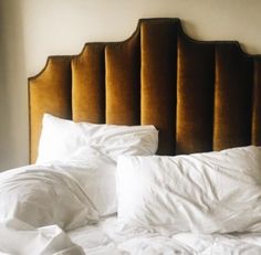 an unmade bed with white sheets and pillows on it's headboard in a bedroom