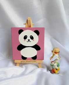 a small easel with a painting of a panda bear on it next to candy