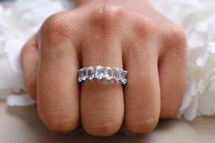 a woman's hand with a wedding ring on her finger and flowers in the background