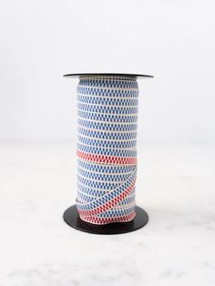 a spool of red, white and blue patterned ribbon on a black stand against a white background