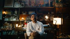 a man sitting in front of a bookshelf filled with lots of books and stuff