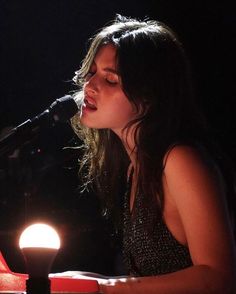 a woman singing into a microphone while sitting at a table with a lit candle in front of her