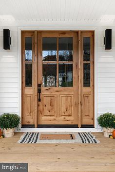 two potted plants sit on the front step of a white house with wooden doors