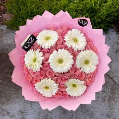 a bouquet of pink roses and white daisies on top of a cement slab with grass in the background