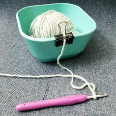 a ball of yarn sitting in a blue bowl next to a pink crochet hook