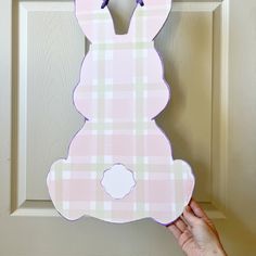 a hand holding up a pink bunny door hanger on a wooden door with plaid pattern