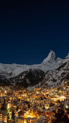 the city is lit up at night in front of snowy mountains and snow - capped peaks