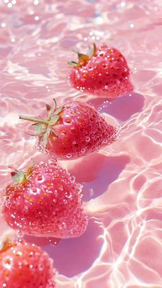 three strawberries floating in the water on a sunny day with bubbles all over them