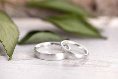 two wedding rings sitting next to each other on top of a white surface with green leaves in the background