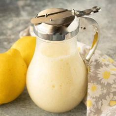 a glass pitcher filled with white liquid next to two lemons and a cloth on the table