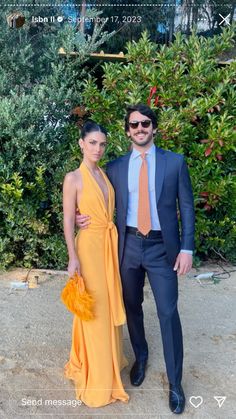 a man in a suit and tie standing next to a woman wearing an orange dress