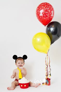 a baby sitting on the floor with mickey mouse cake and balloons in front of him