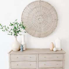 a white dresser with some vases on top of it next to a wall hanging