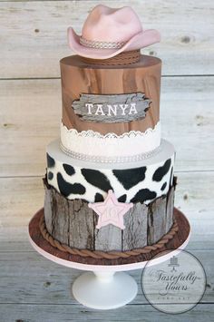 a three tiered cake decorated with cow print and pink cowboy hat, on top of a white pedestal