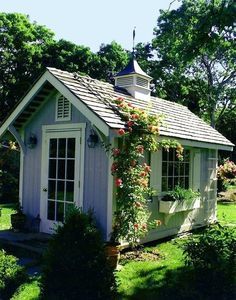 a small white shed sitting in the middle of a lush green yard with flowers growing on it