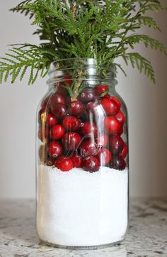 a glass jar filled with red berries and pine cones