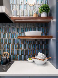 a kitchen with blue and white tile backsplashing, wooden shelves and tea kettle on the counter