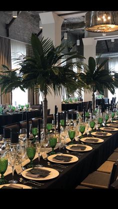 a long table is set up with place settings and palm trees in the centerpieces