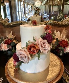 a three tiered white cake with flowers on the top and side, in front of a mirror