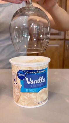 a person pours vanilla ice cream into a cup with a plastic lid on the counter