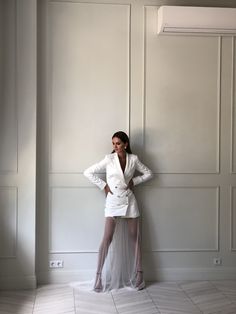 a woman in a white suit leaning against a wall with her hands on her hips