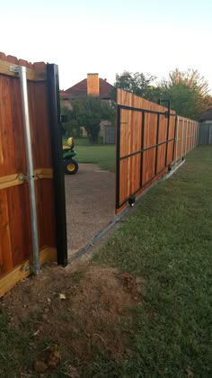 a wooden gate is opened to allow people to enter the yard from behind it, with a tractor in the background