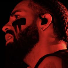 a bearded man with ear piercings on his ears looking to the side in red light