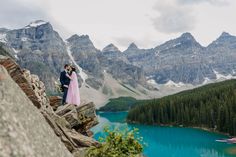 a man and woman standing on top of a mountain next to a lake