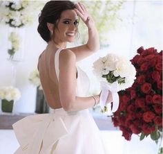 a woman in a white dress holding a bouquet of red and white flowers with her hand on her head