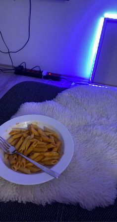 a white plate topped with pasta on top of a bed next to a laptop computer