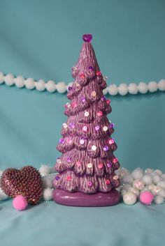 a small purple christmas tree sitting on top of a table next to balls and beads