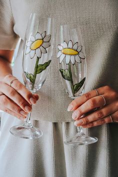 two wine glasses with daisies painted on them are being held by someone's hands