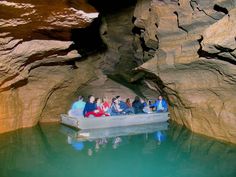 people are sitting on a boat in the middle of a cave with water and rocks