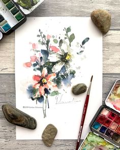 watercolors and rocks on a wooden table with flowers