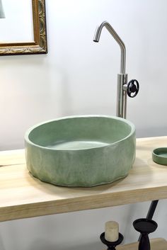 a green bowl shaped sink sitting on top of a wooden counter next to a mirror