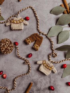 Handmade sweater garland with tan sweaters and brown pants hung on garland with little white wire hangers. Garland string is brown and tan with brown and cream pom poms on each end of the garland. Garland is seen on a concrete counter with cranberries, cinnamon sticks, and greenery. Christmas Tapestry Wall Hangings, Knit Sweater Ornament, Knitted Garland Christmas, Cozy Christmas Mantle, Knitting Christmas Ornaments, Christmas Crochet Garland, Knit Garland, Knitted Garland, Knitted Christmas Ornaments